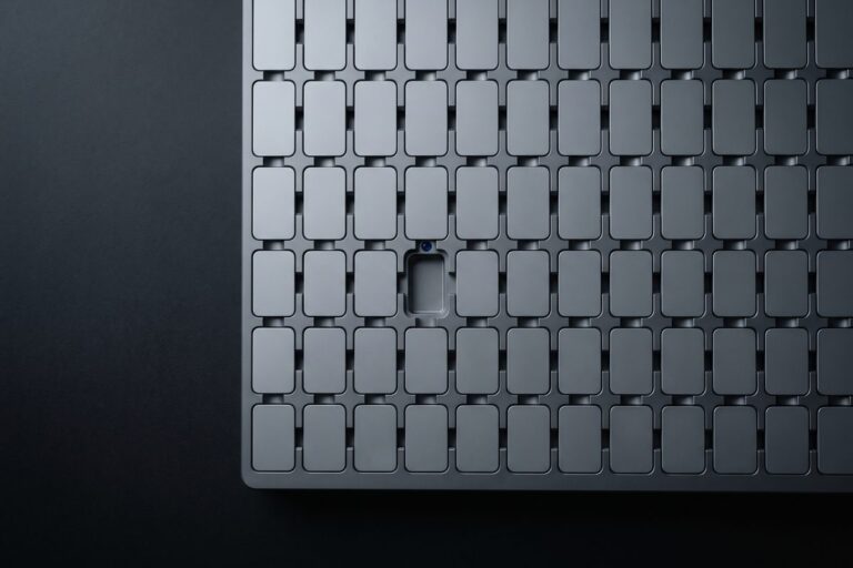 Grid of matte gray plates in a machined tray running past the frame edges, one slot empty with a single blue lens on its rim